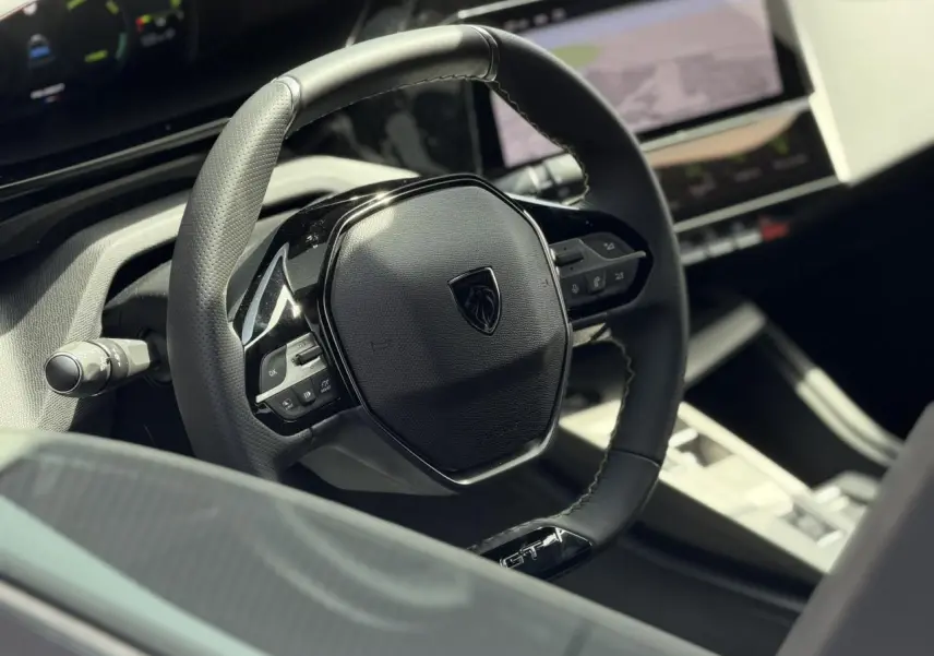 Vue rapprochée du volant cuir noir GT du Peugeot 308 NV Hybrid 145 GT avec tableau de bord numérique et écran tactile.