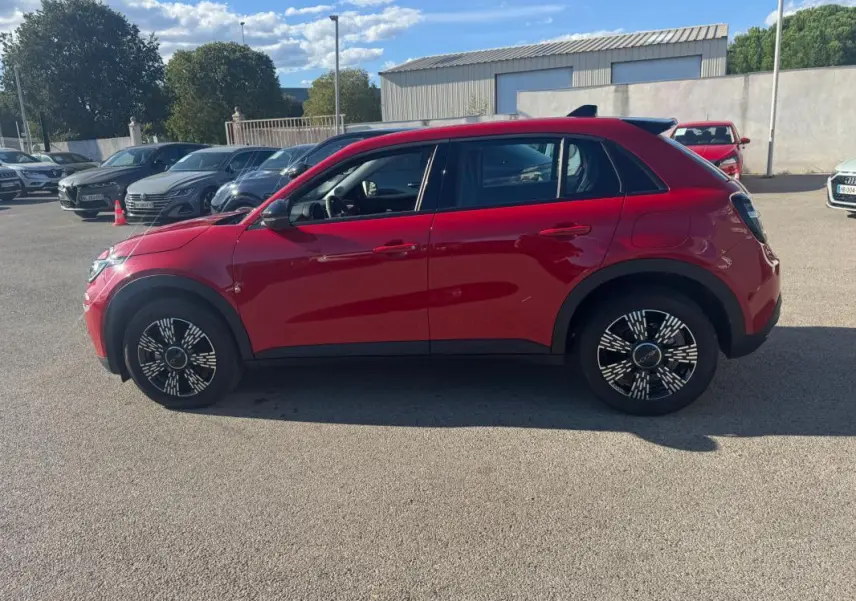 Vue latérale gauche d'une FIAT 600 T-Gen 3 rouge de 2025 avec jantes au design moderne, stationnée en extérieur.