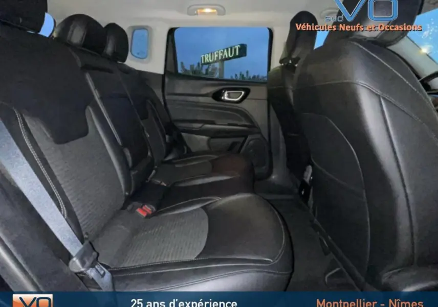 Vue intérieure arrière du Jeep Compass 2021 noir, sièges en cuir et tissu avec accoudoir central et ceintures visibles.