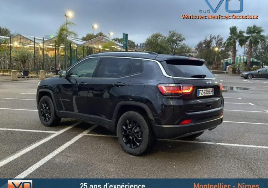 Vue 3/4 arrière droite d'un Jeep Compass noir avec jantes alliage noires et barres de toit sur parking extérieur.