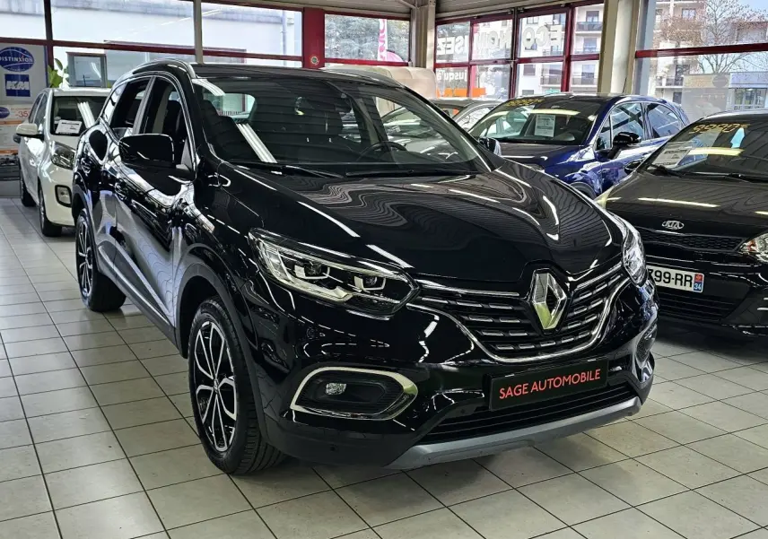 Renault Kadjar noir en 3/4 avant droit dans un showroom, avec jantes bi-ton et calandre chromée visible.