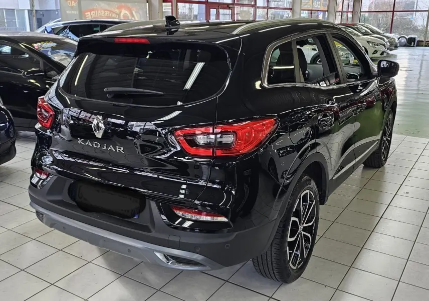 Vue 3/4 arrière droite d'un Renault Kadjar noir brillant avec feux arrière LED et jantes bi-ton en showroom.