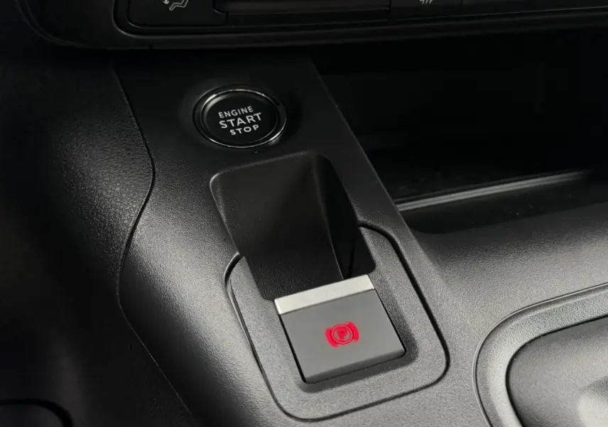 Gros plan sur la console centrale du Peugeot Rifter gris acier, montrant le bouton de frein de stationnement électrique et démarrage moteur.