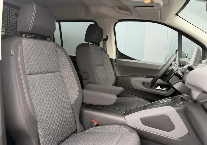 Vue intérieure côté conducteur du Peugeot Rifter gris acier 2026, sièges tissu gris avec accoudoirs et tablette tactile visible.