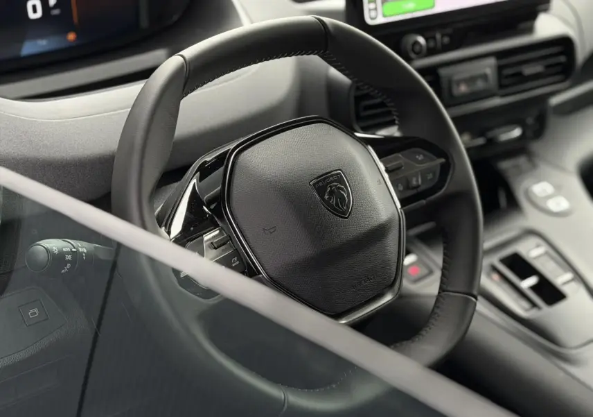 Gros plan sur le volant cuir noir du Peugeot Rifter 2026 avec commandes intégrées et tableau de bord numérique partiel.