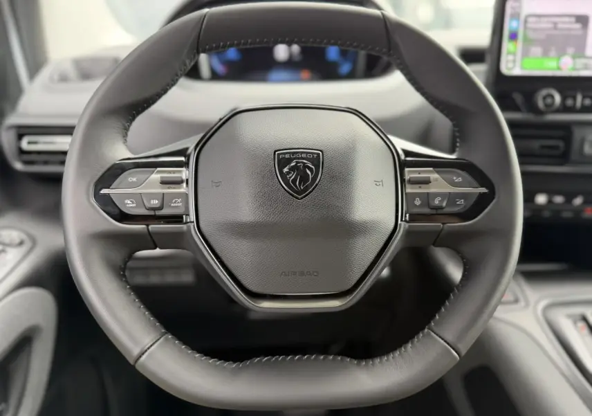 Volant cuir multifonction Peugeot Rifter vu de face avec commandes intégrées et tableau de bord flou en arrière-plan.