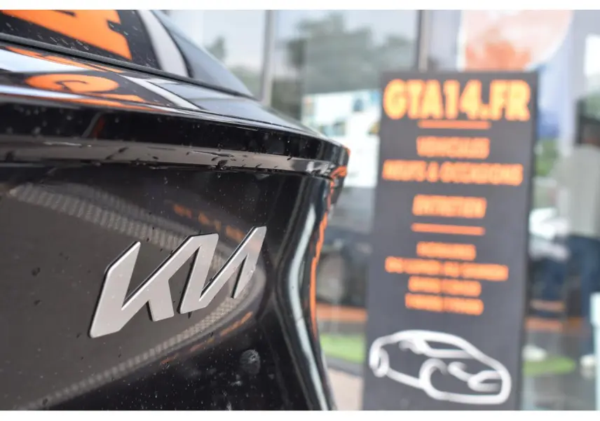 Gros plan sur le logo KIA à l'arrière d'un SUV noir, avec un panneau flou en arrière-plan.