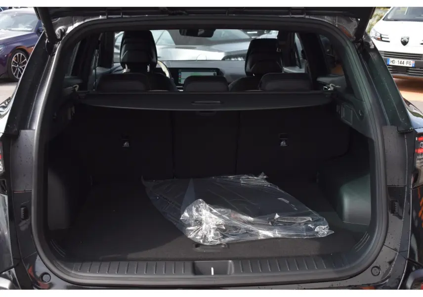 Coffre ouvert vu de l'arrière d'un KIA Sportage noir 2026, intérieur spacieux avec tapis plastique transparent.