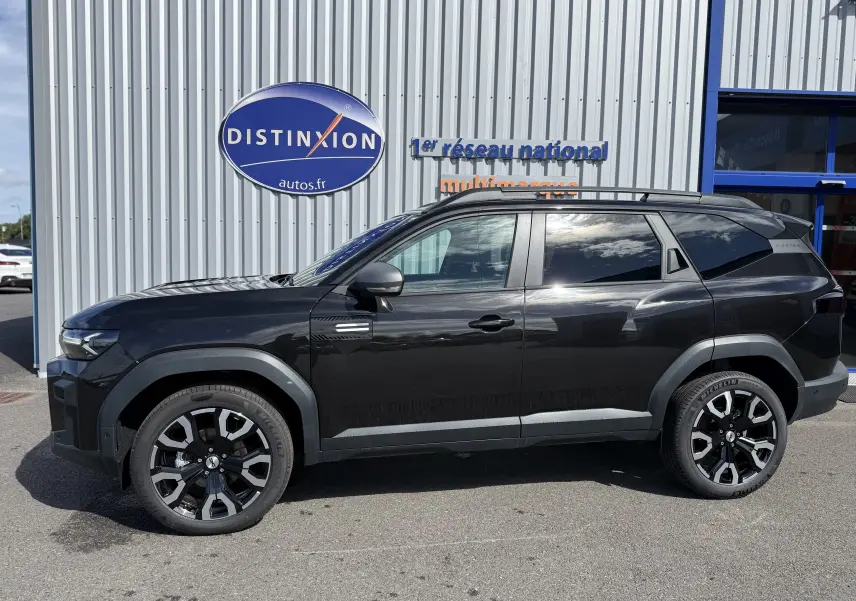 Profil droit du SUV Dacia Bigster Hybrid 155 Journey noir nacré avec jantes biton 19 pouces, garé devant un mur métallique.