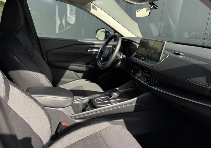 Intérieur côté conducteur du Nissan Qashqai 2025, sellerie mixte noire, tableau de bord moderne avec écran tactile central.