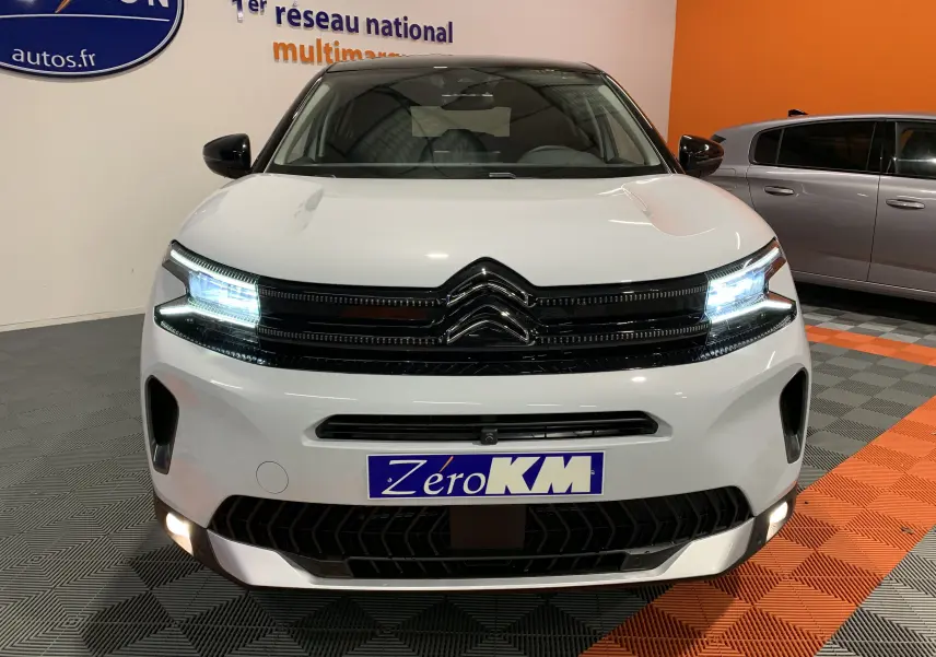 Vue avant du Citroën C5 Aircross hybride blanc 2024 avec phares LED allumés et calandre noire brillante.