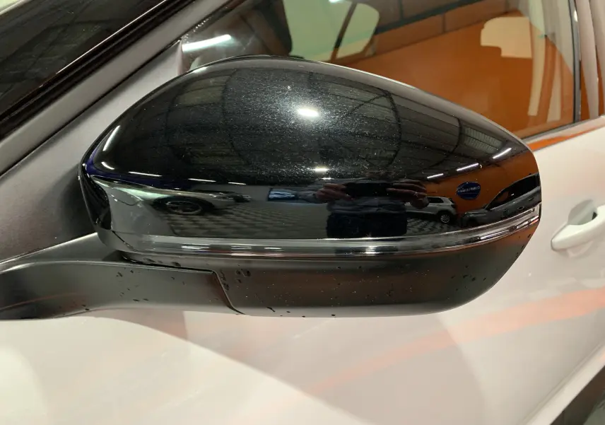 Rétroviseur noir brillant côté gauche du Citroën C5 Aircross Hybride blanc 2024, reflet intérieur orange visible.