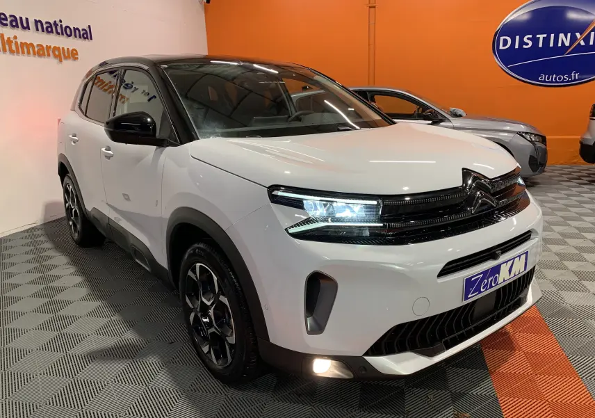 Citroën C5 Aircross hybride blanc vue 3/4 avant droit avec phares LED allumés en intérieur showroom.