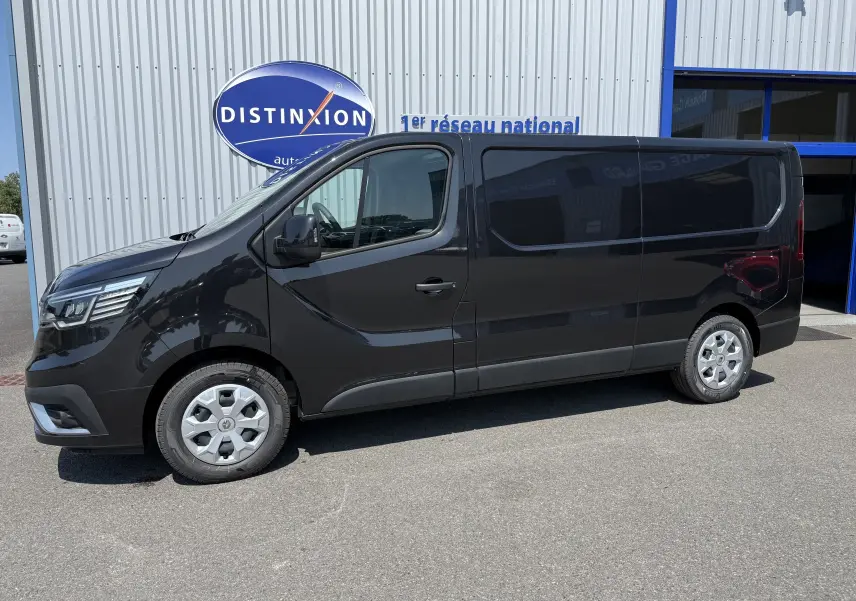 Renault Trafic Fourgon noir crépuscule métal vu de profil côté gauche, stationné devant un bâtiment commercial.