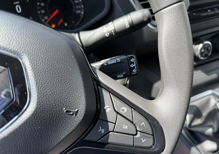 Gros plan sur le volant gris du Renault Trafic Fourgon 2025 avec commandes multifonctions et tableau de bord en arrière-plan.