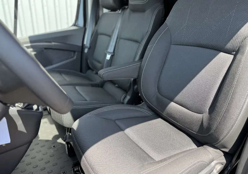 Vue rapprochée des sièges avant noirs en tissu du Renault Trafic Fourgon L2H1, avec accoudoir côté conducteur.