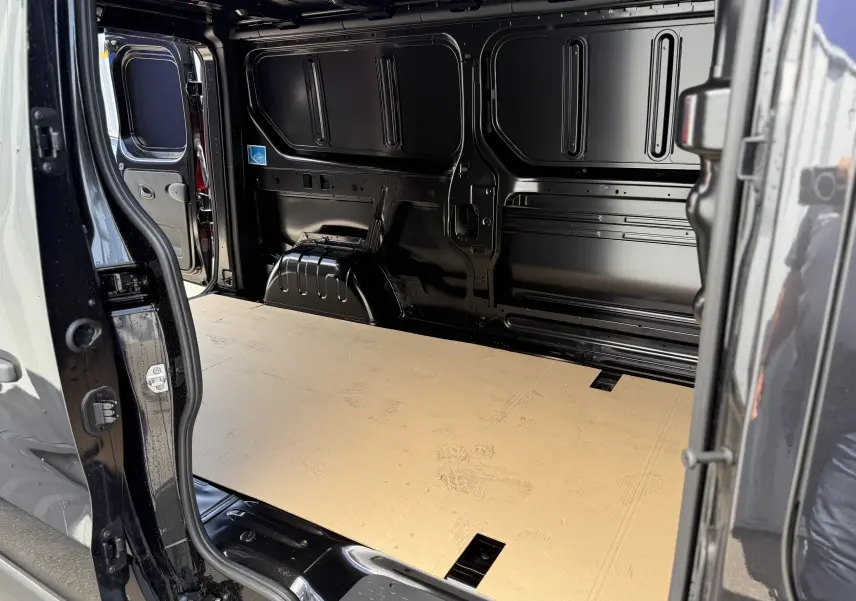 Intérieur du fourgon Renault Trafic noir crépuscule, vue latérale gauche sur l'espace de chargement vide et plancher beige.