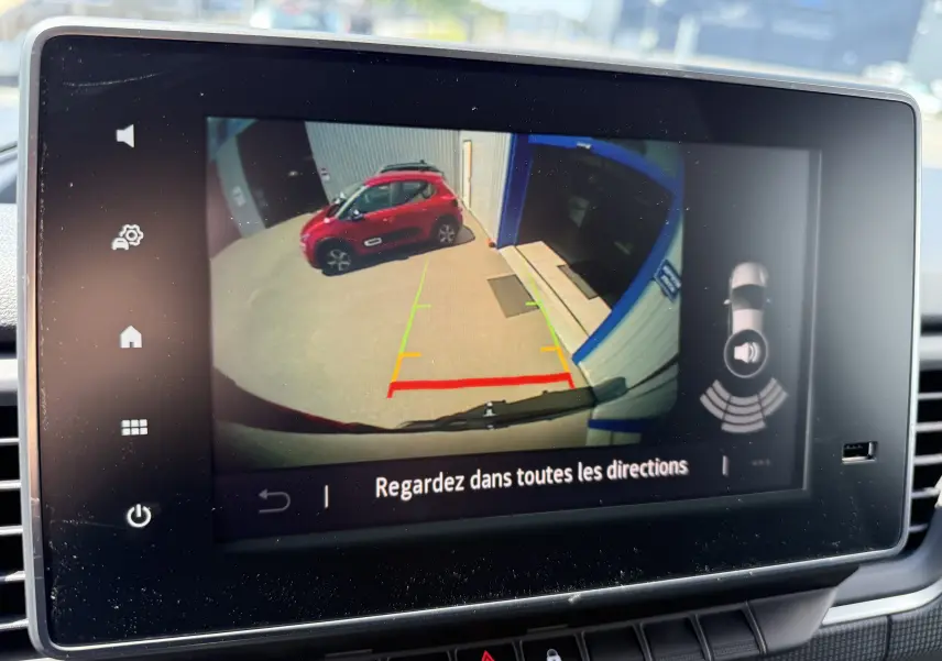 Vue arrière depuis la caméra de recul du Renault Trafic noir crépuscule, avec un véhicule rouge visible à gauche.