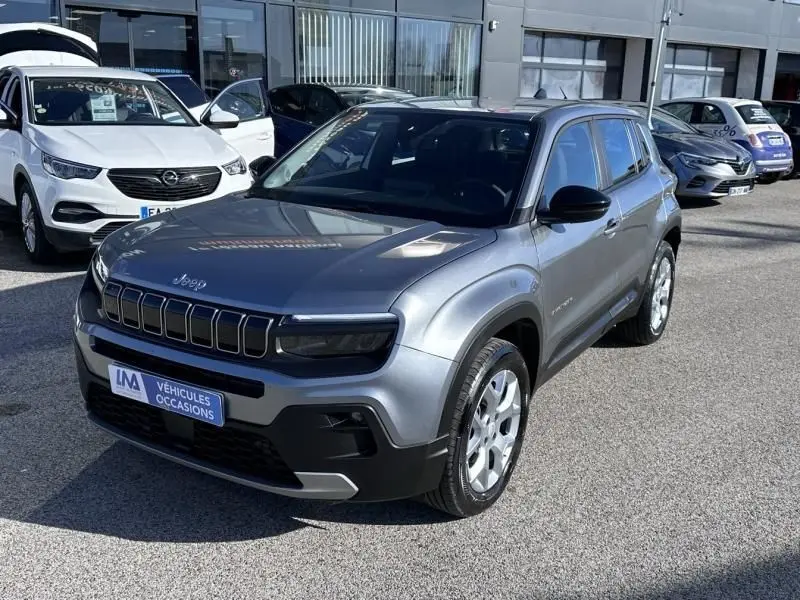 Jeep Avenger gris métallisé en 3/4 avant droit, avec calandre noire distinctive et toit noir contrasté.