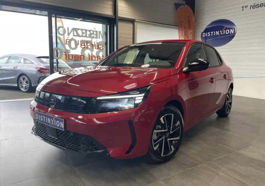 Opel Corsa rouge vue 3/4 avant droit en intérieur, calandre noire et jantes alliage diamantées.