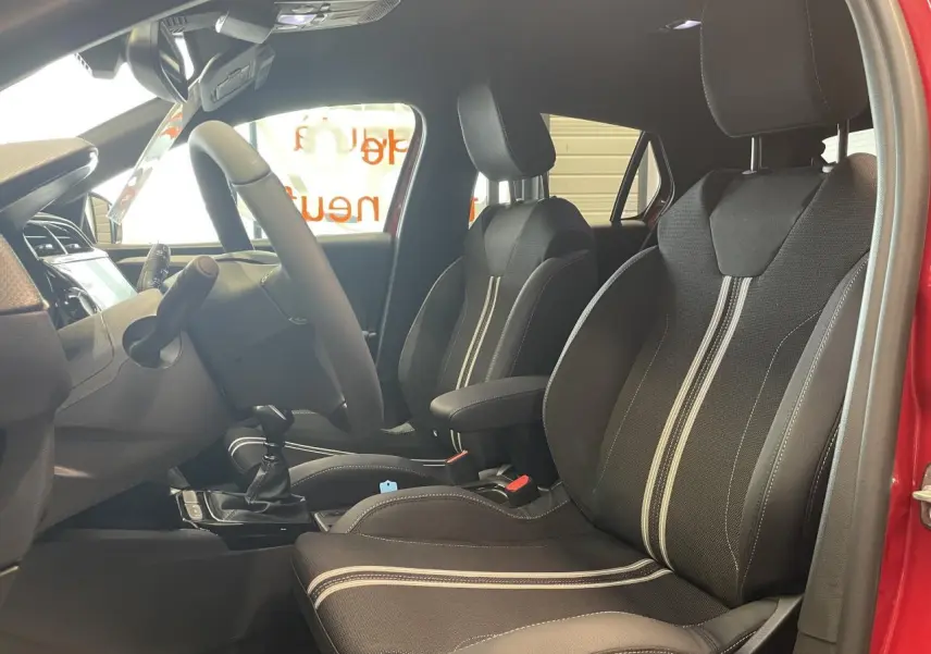 Intérieur avant de l’Opel Corsa rouge 2026, vue côté conducteur montrant sièges sport noirs avec bandes blanches.