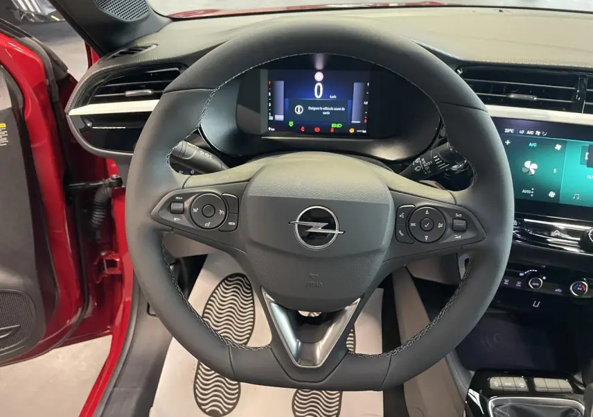 Vue intérieure centrée sur le volant noir de l'Opel Corsa rouge avec tableau de bord numérique et écran tactile.