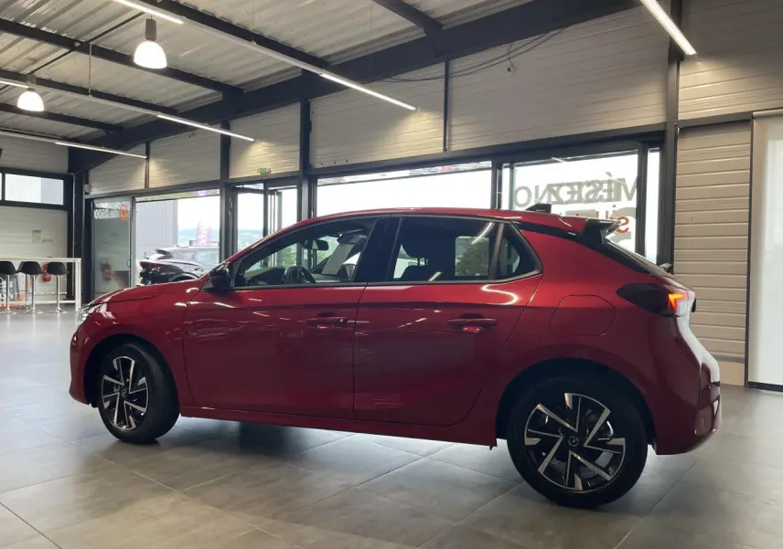 Opel Corsa rouge vue de profil côté gauche en intérieur, avec jantes alliage et toit couleur carrosserie.