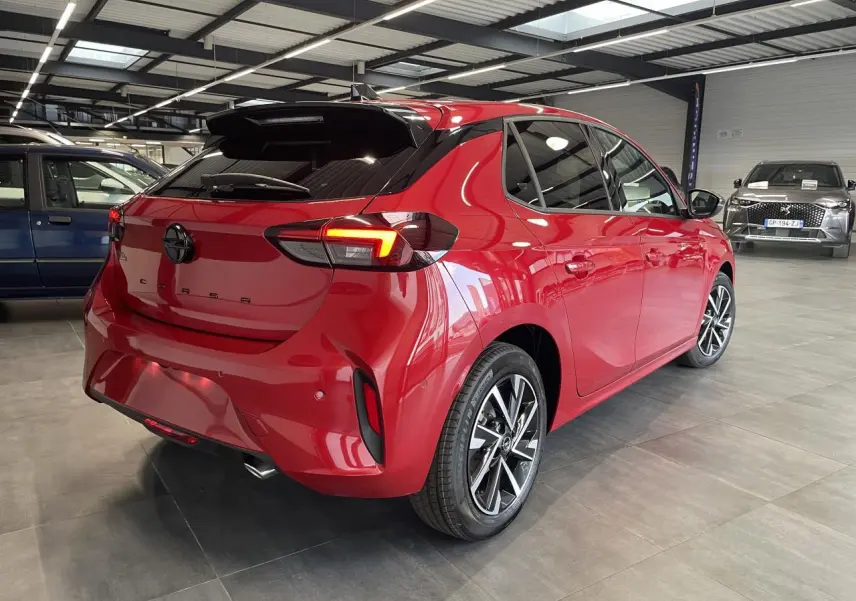 Vue 3/4 arrière droite d'une Opel Corsa rouge métallisée avec jantes alliage et vitres arrière surteintées en showroom.