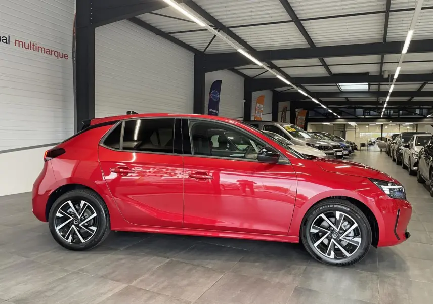 Opel Corsa rouge vue de profil côté gauche en intérieur, avec jantes alliage et vitres surteintées.