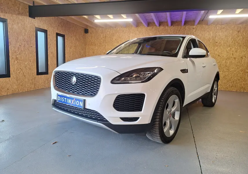 Jaguar E-PACE blanc en vue 3/4 avant droit, avec calandre distinctive et phares LED dans un garage.