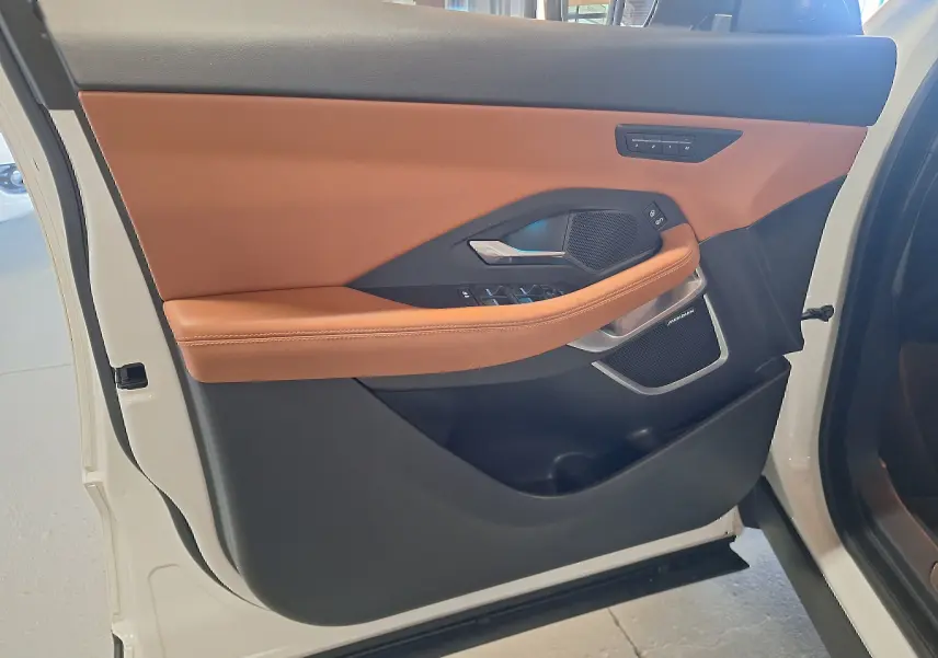 Vue intérieure de la porte avant gauche blanche du Jaguar E-PACE 2019 avec garniture cuir marron et haut-parleur Meridian.