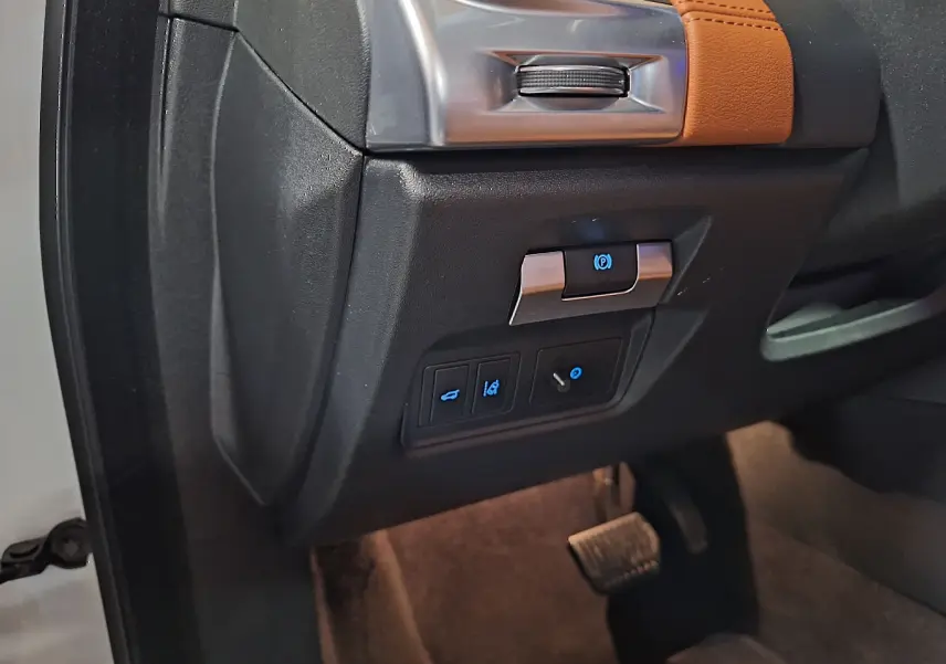 Détail intérieur côté gauche du tableau de bord du Jaguar E-PACE blanc, avec commandes éclairées et pédale visible.