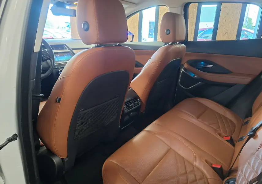 Vue intérieure arrière droite du Jaguar E-PACE blanc 2019, sièges en cuir marron avec surpiqûres et console centrale visible.
