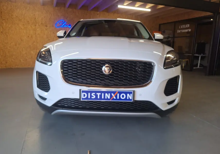 Vue frontale d'un Jaguar E-PACE blanc 2019 avec calandre noire et phares LED dans un garage.