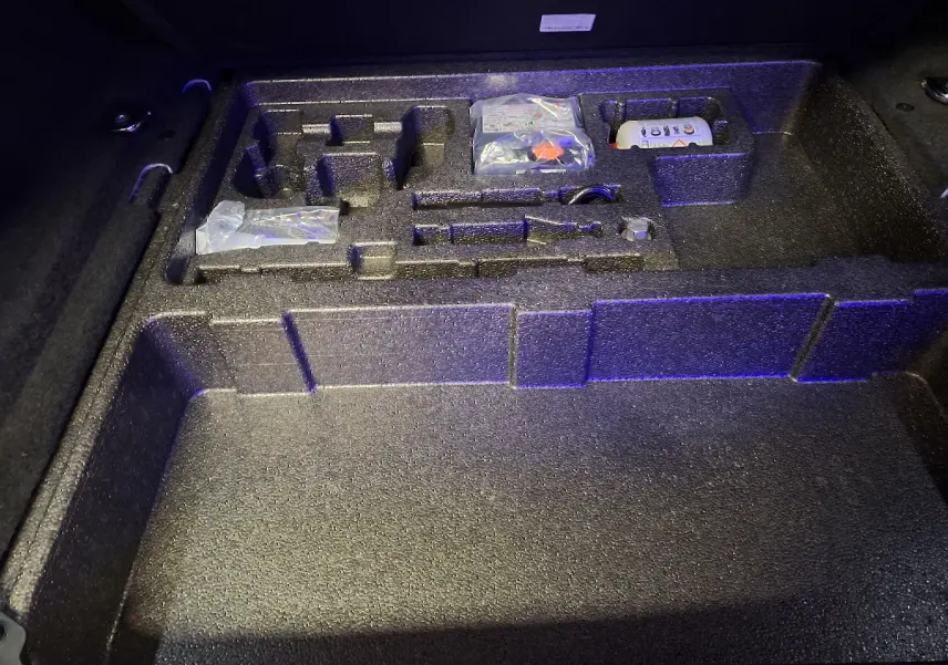 Coffre ouvert du Jaguar E-PACE blanc 2019, vue plongeante sur le rangement en mousse avec outils et accessoires.