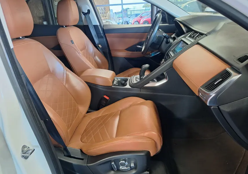 Vue intérieure côté conducteur du Jaguar E-PACE blanc 2019, sièges cuir marron et tableau de bord assorti.