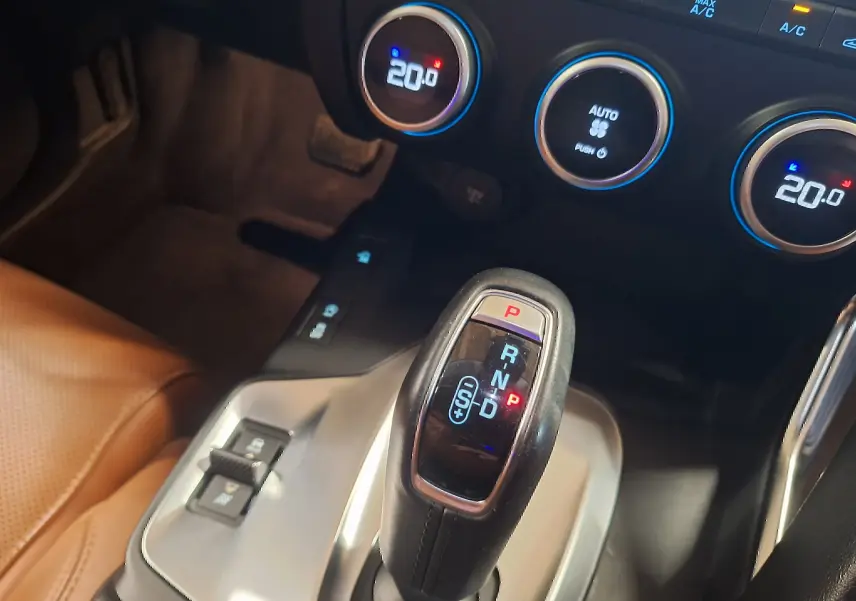 Gros plan sur le levier de vitesses automatique noir et argenté dans l’habitacle du Jaguar E-PACE blanc, avec commandes climatisation visibles.