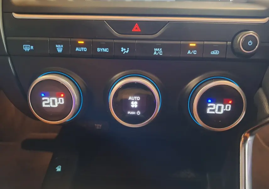 Gros plan sur les commandes de climatisation digitale à 20°C du Jaguar E-PACE blanc, avec boutons ronds et affichages lumineux.