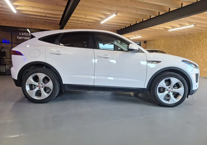 Jaguar E-PACE blanc vue de profil côté gauche, stationné en intérieur avec jantes alliage visibles.