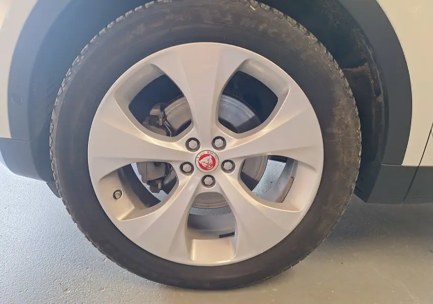 Gros plan sur la roue avant droite blanche d'une Jaguar E-PACE 2019, jante alliage avec logo Jaguar rouge au centre.