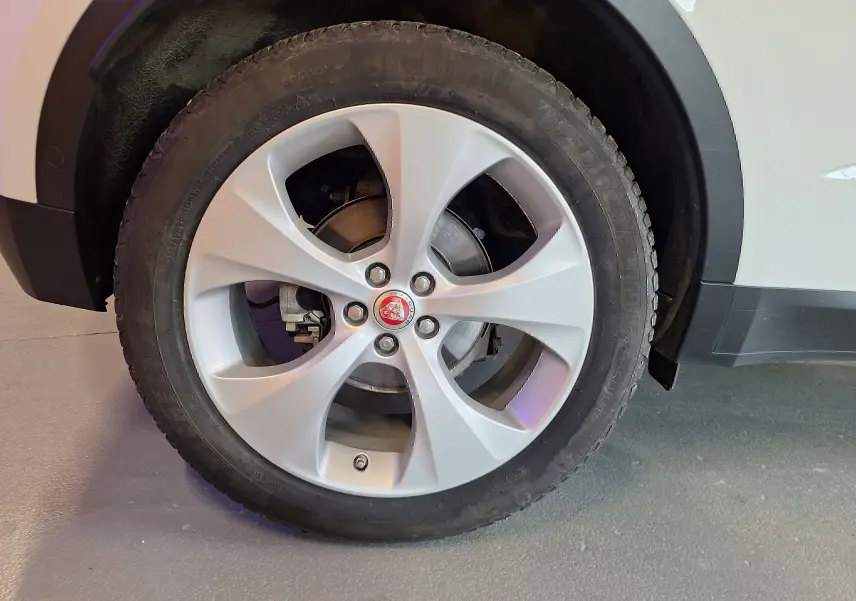 Gros plan sur la roue avant droite argentée avec logo Jaguar sur un Jaguar E-PACE blanc.
