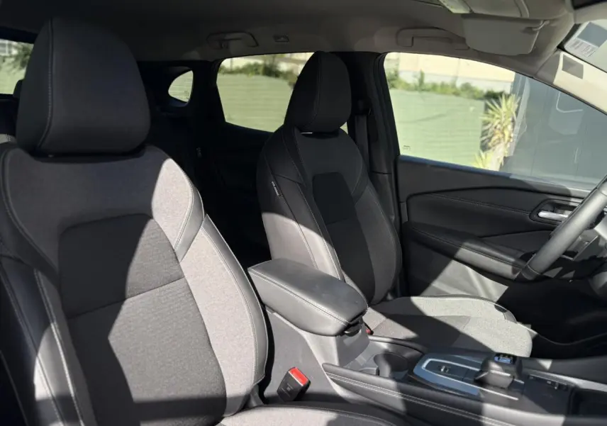 Intérieur du Nissan Qashqai 2025 montrant les sièges avant gris et la console centrale avec accoudoir et levier de boîte automatique.