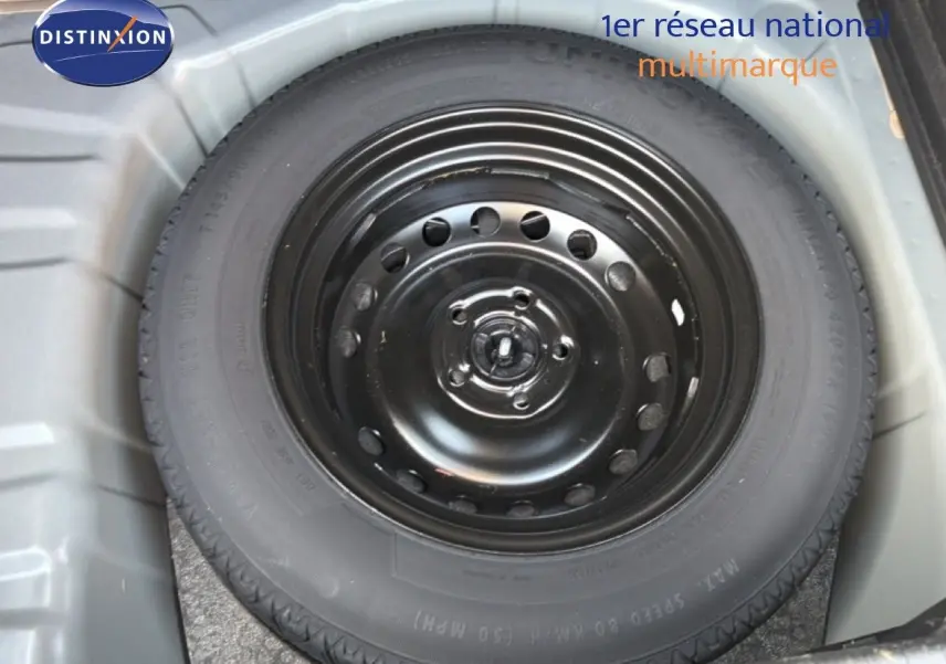 Roue de secours noire dans le coffre d’un Renault Captur bleu marine fumé, vue en plongée.