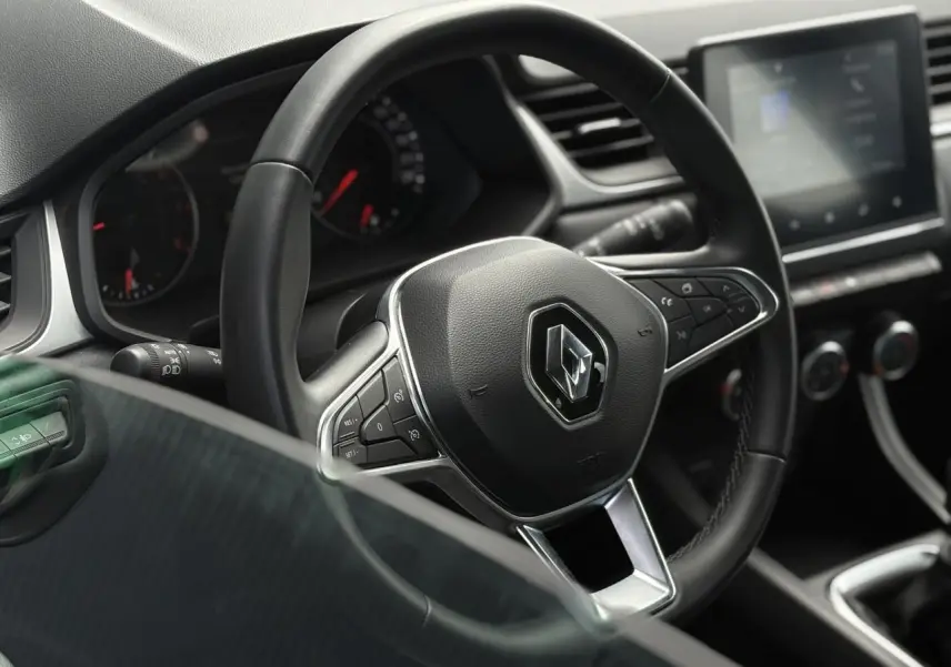 Vue rapprochée du volant noir du Renault Captur 2022 avec commandes intégrées et tableau de bord numérique flou.