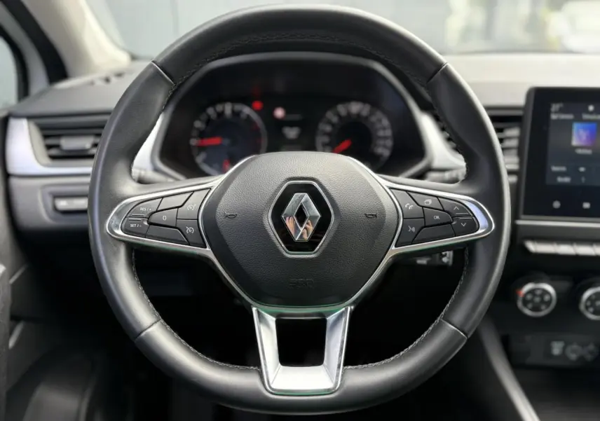 Volant en cuir noir de Renault Captur 2022 avec commandes intégrées et tableau de bord flou en arrière-plan.