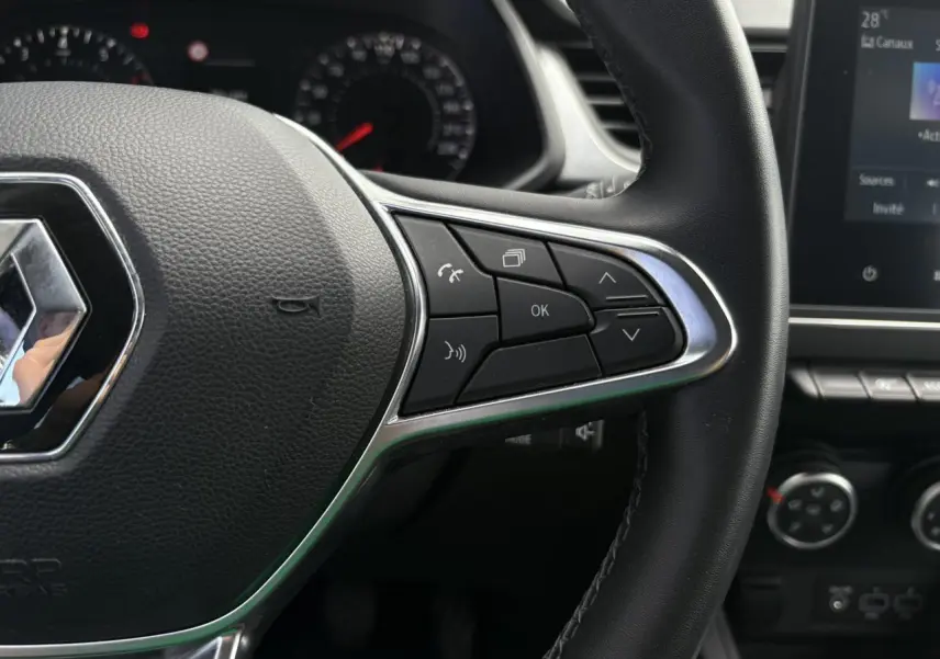 Gros plan sur le volant noir du Renault Captur 2022 avec commandes multifonctions et tableau de bord partiellement visible.