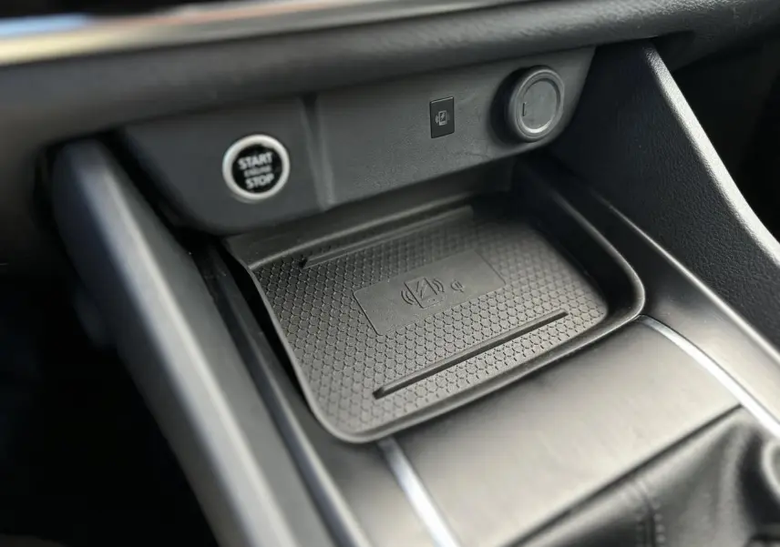 Gros plan sur la console centrale noire du Nissan Qashqai 2024, avec zone de recharge sans fil et bouton Start/Stop.