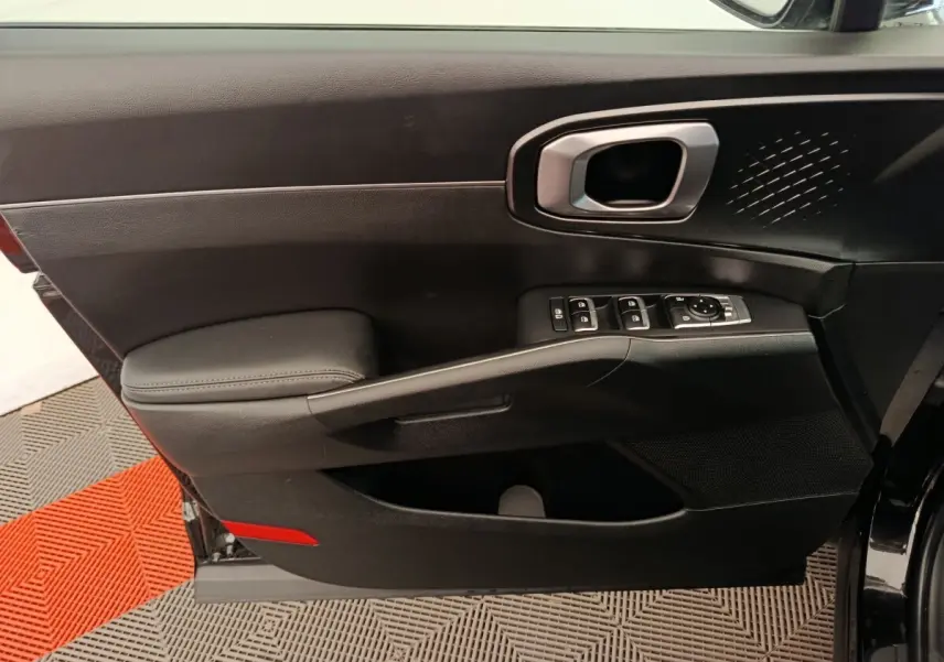 Vue intérieure côté gauche de la porte avant noire du Kia Sorento 2023 avec commandes électriques et poignée argentée.