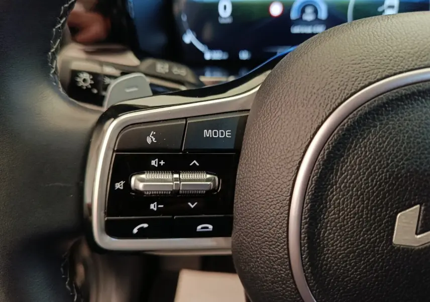 Gros plan sur les commandes gauche du volant cuir noir du KIA Sorento 2023 hybride rechargeable, avec boutons multifonctions.