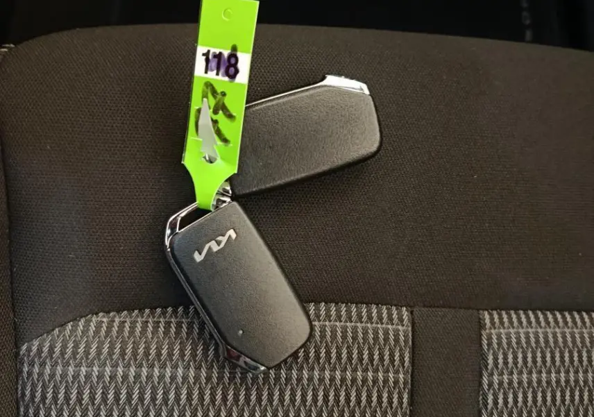 Clé noire KIA posée sur siège tissu gris à motifs, vue rapprochée sans angle de véhicule visible.